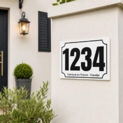 Plaque numéro maison personnalisée blanche avec numéro noir fixée sur un pilier de portail devant une maison