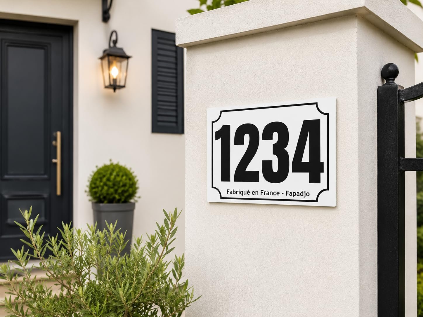 Plaque numéro maison personnalisée blanche avec numéro noir fixée sur un pilier de portail devant une maison